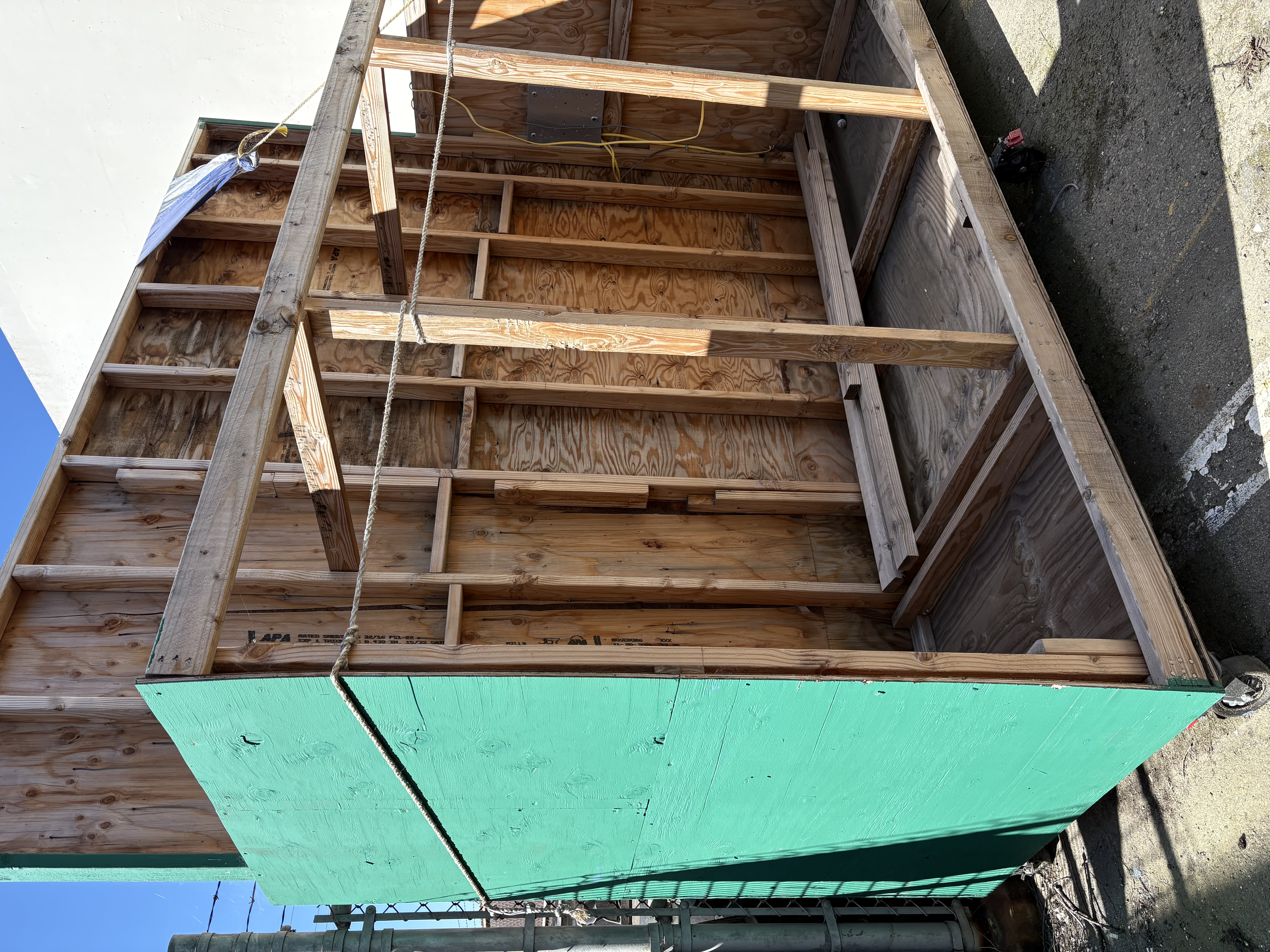 Wood structure with wheels, exterior green paint. Item is taller than barbed wire fence, and about the size of a small stage.
