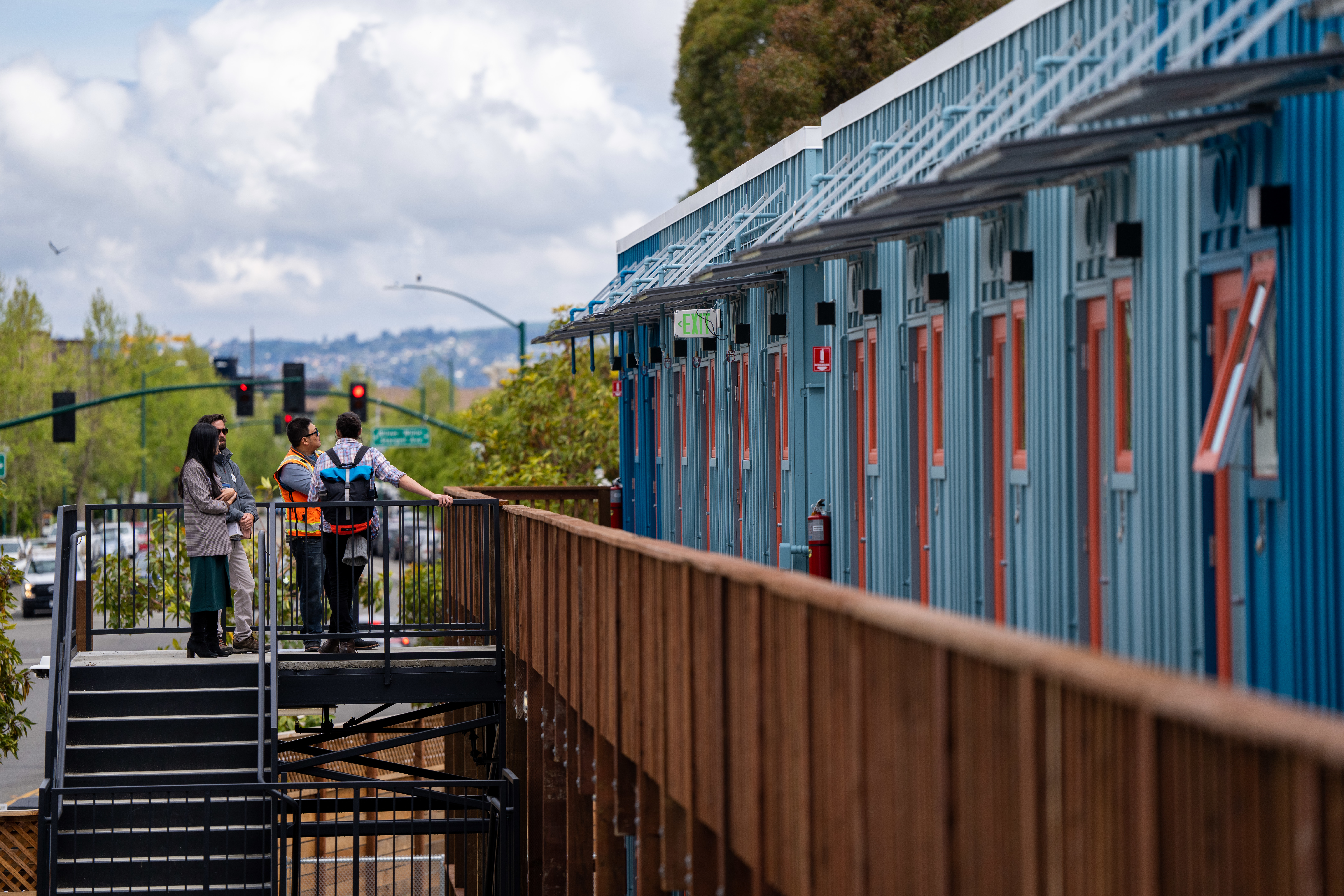 Side view of a row of cheerful, small apartments made of recycled shipping containers with some construction workers in the background.